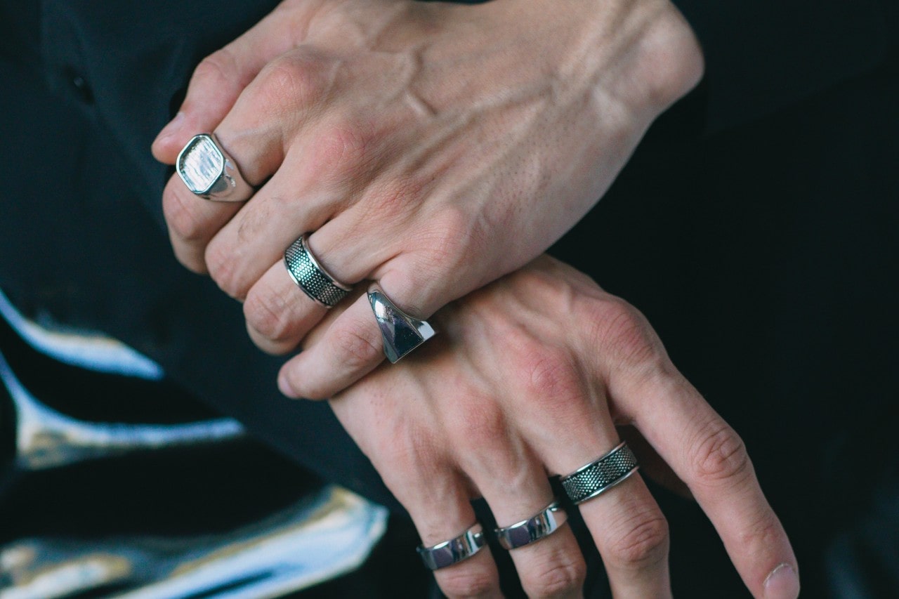 a pair of hands wearing stack of thick, silver fashion rings