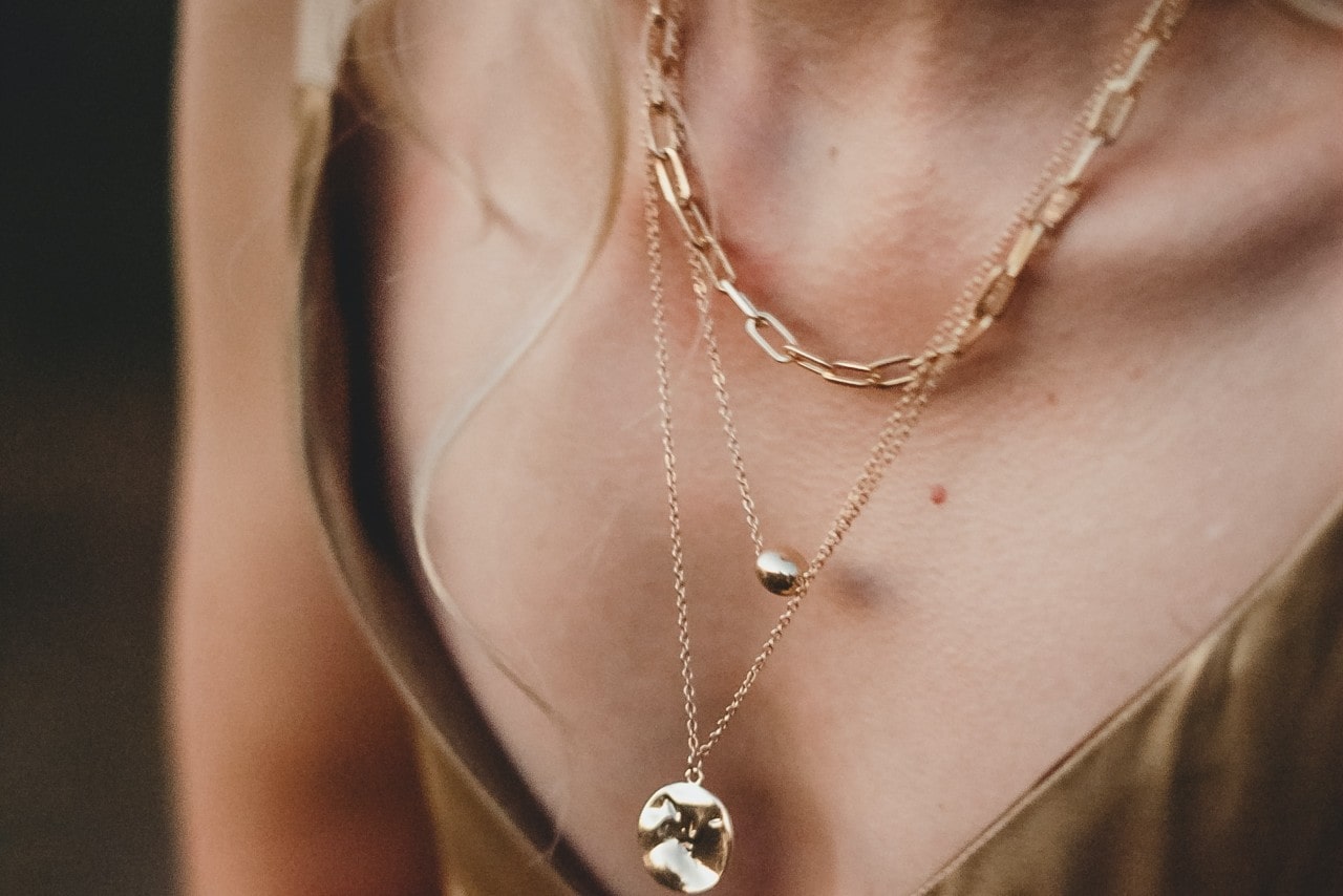 close up image of a woman wearing three layered yellow gold necklaces.