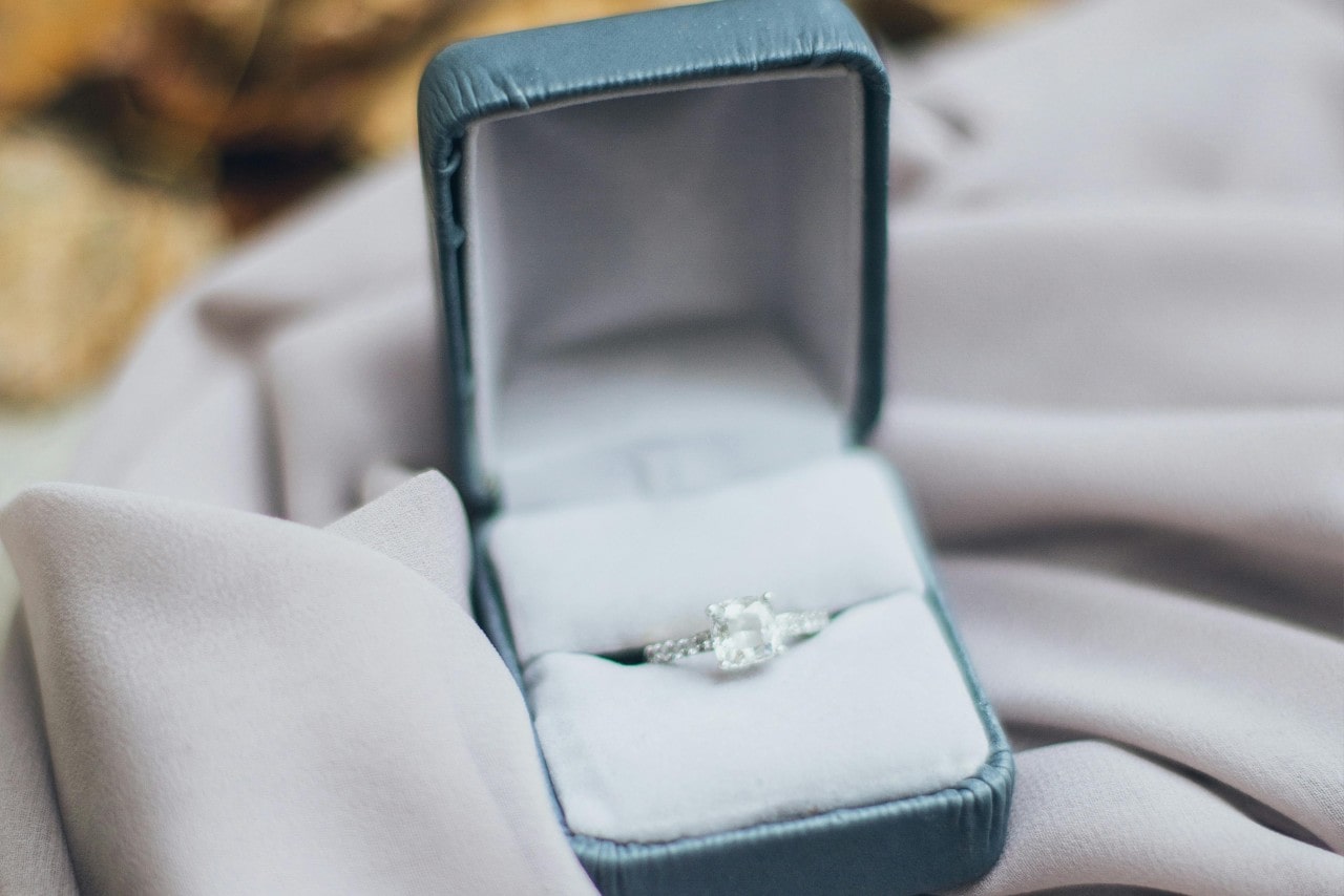 A close-up of a white gold princess cut diamond engagement ring in a blue ring box.