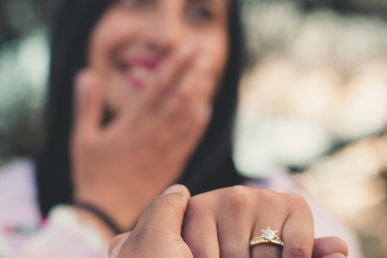 A close-up of a man holding a woman’s hand adorned with a yellow gold diamond side stone engagement ring.