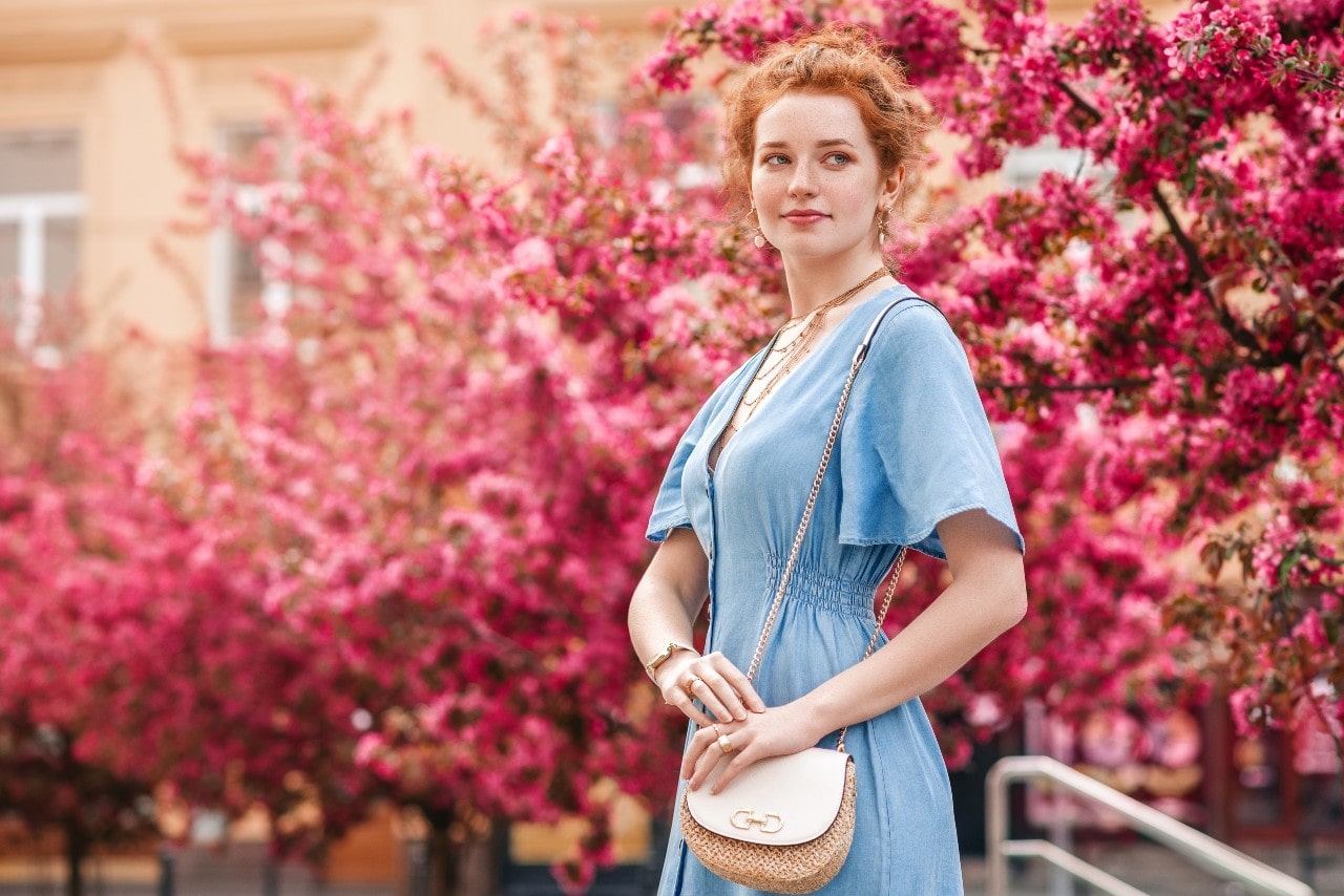 A woman in a blue dress walks through a park with blooming trees.