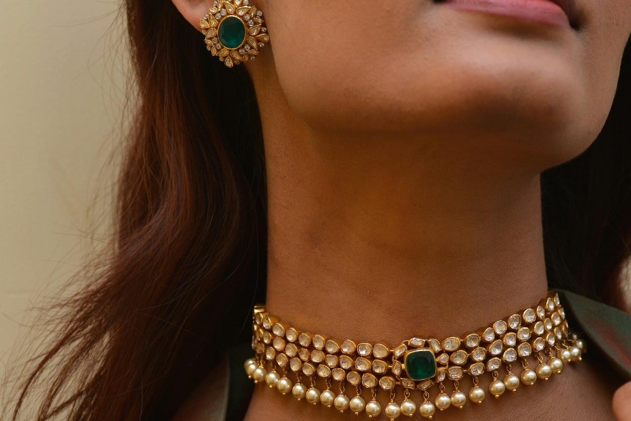 Close-up of a woman's neck adorned with a gold choker necklace featuring pearls and a green gemstone.