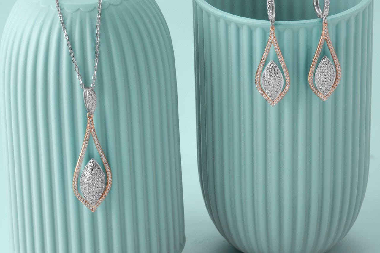a set of mixed metal diamond jewelry, a necklace and earrings, hanging on blue vases