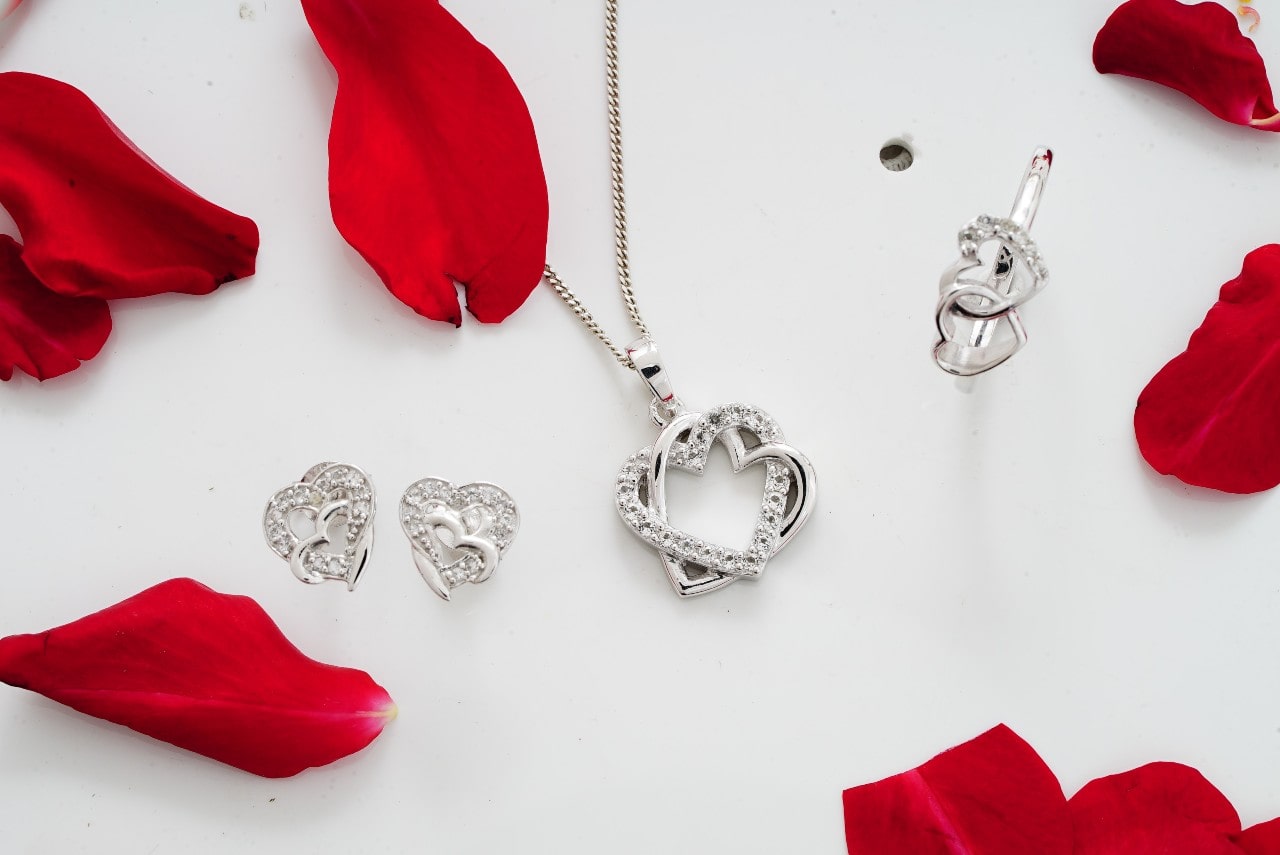 set of white gold diamond jewelry featuring heart motifs on a white background with rose petals