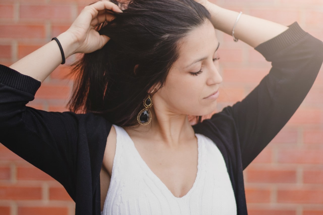 a woman stretches while walking, showcasing her onyx drop earrings.