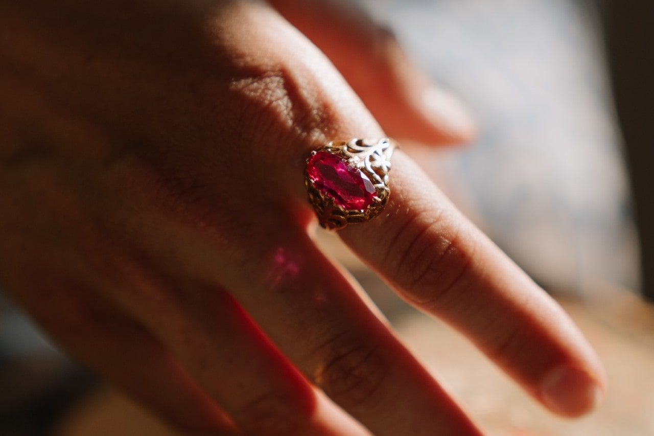 close up image of a hand adorned with a yellow gold fashion ring featuring a pink center stone