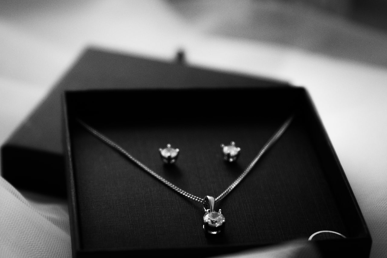A close up of a silver diamond pendant necklace and stud diamond earring set in a black box.