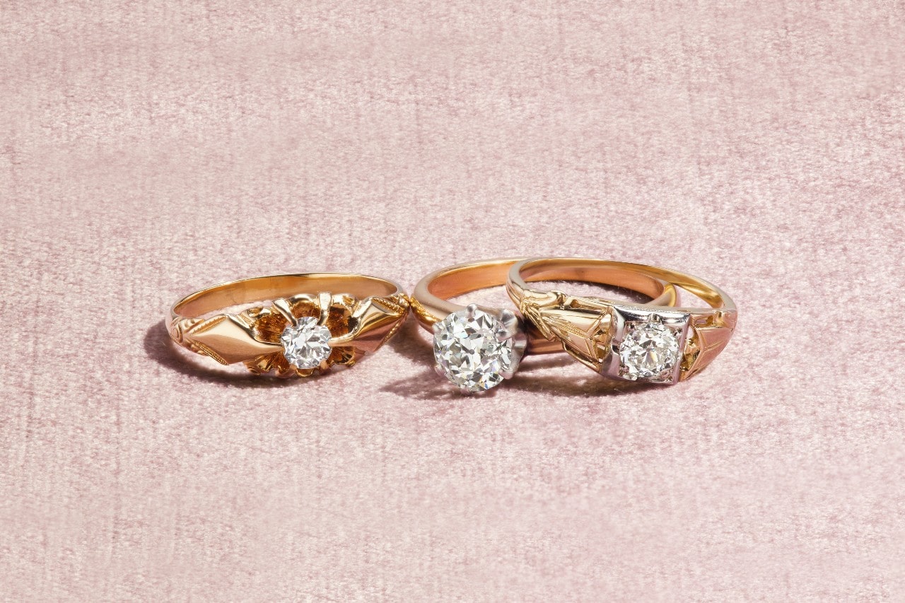 Three yellow gold rings with distinctive diamond settings rest on a textured pink surface