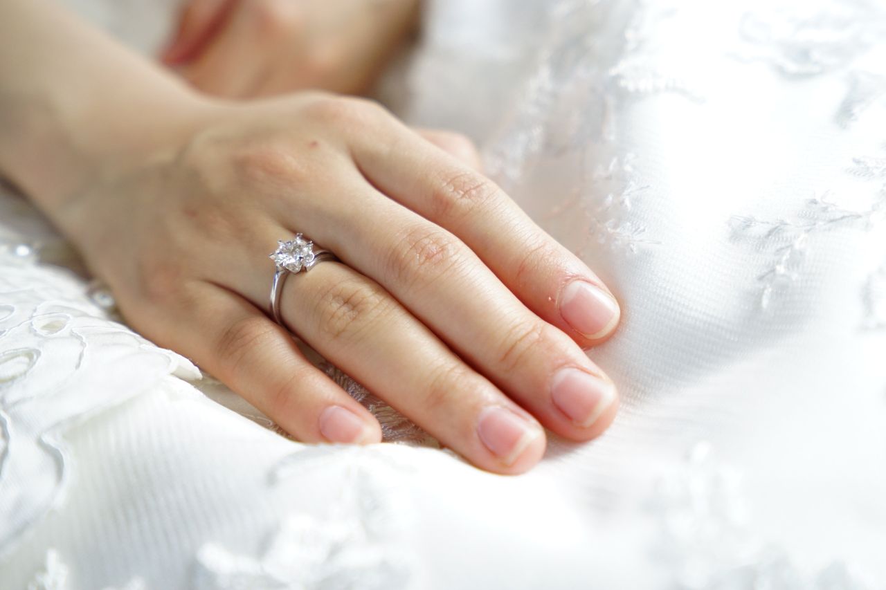 A woman resting her hand on a white gown with a floral print, her solitaire engagement ring shining in the light.