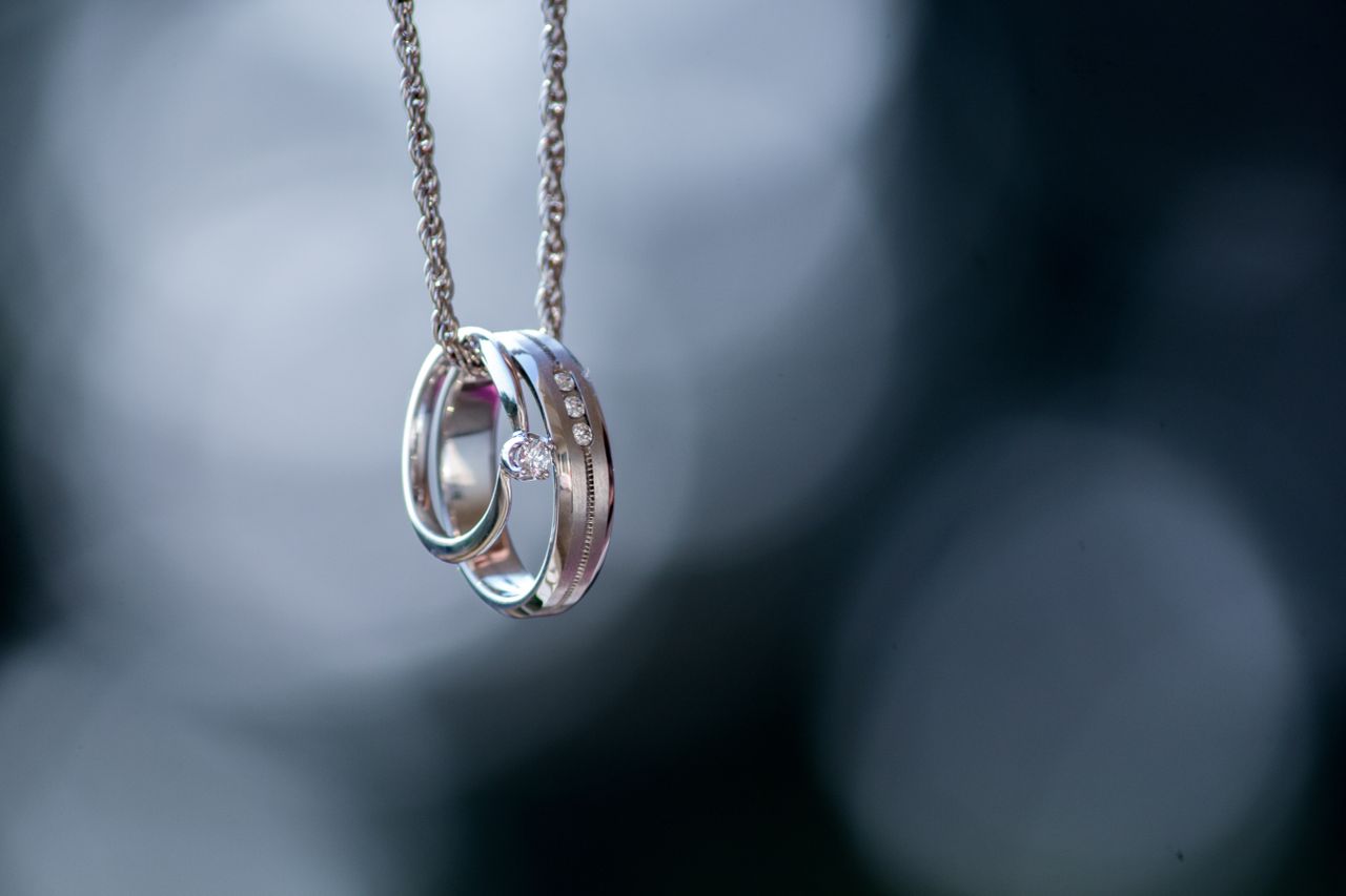 A solitaire engagement ring and a wedding band hanging on a silver chain with a blurred background.
