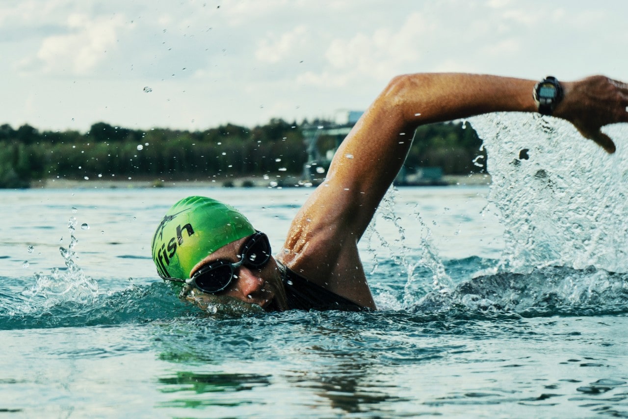 Man swimming through the water and has a watch on his wrist as he does the breaststroke.