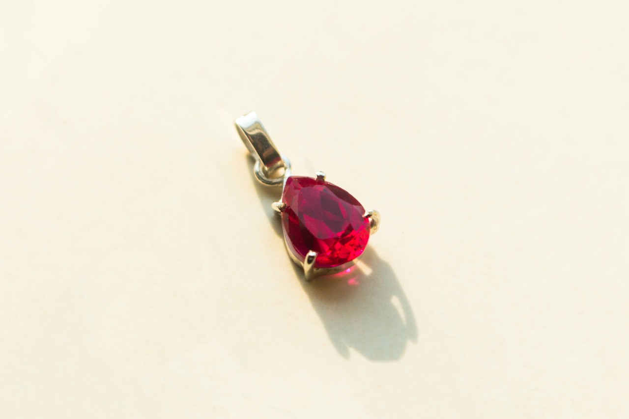 A close up of a pear-shaped ruby pendant on a white surface.
