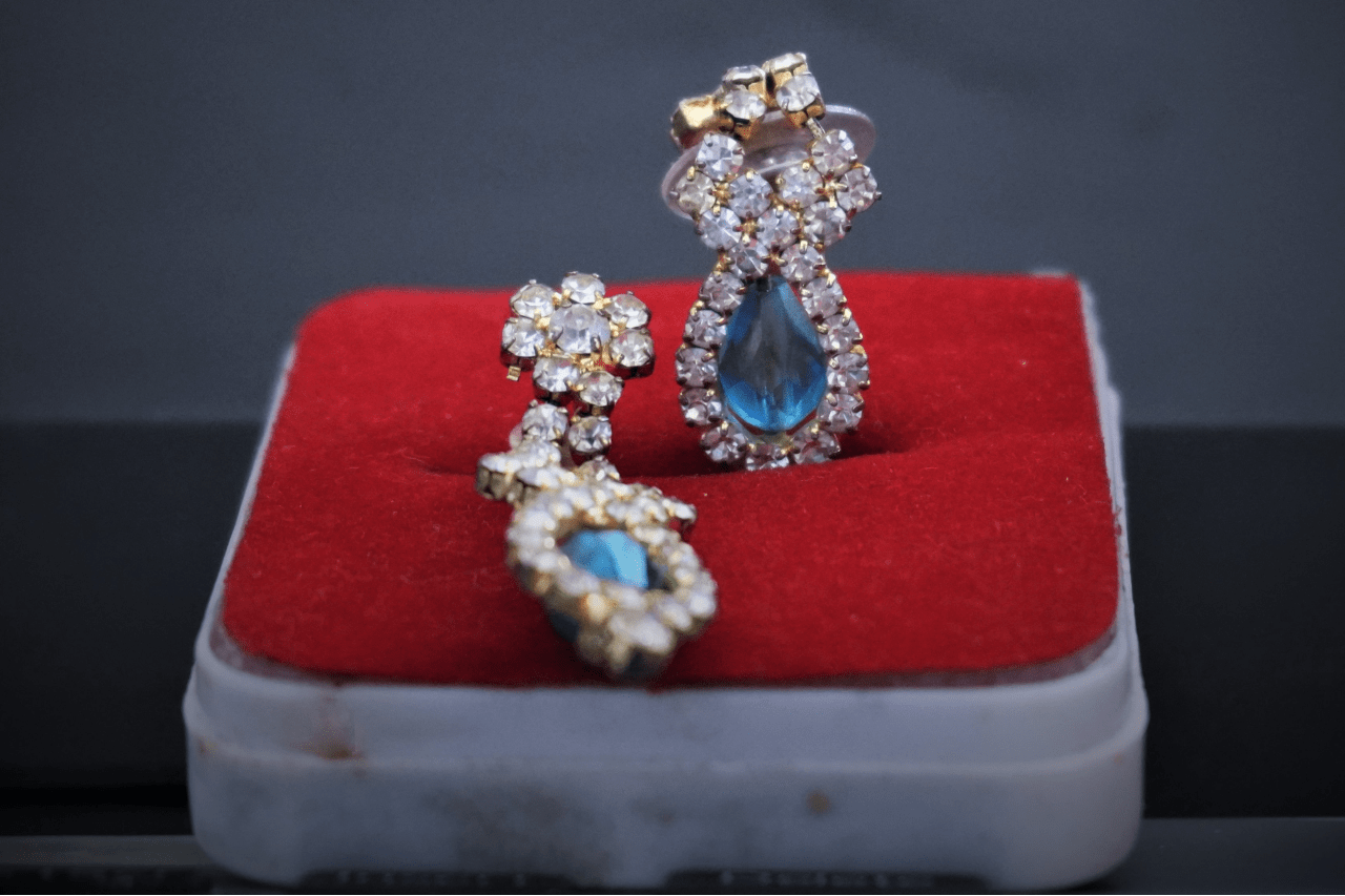 A pair of elegant gold earrings with teardrop-shaped blue gemstones surrounded by clear crystals displayed on a red velvet box.