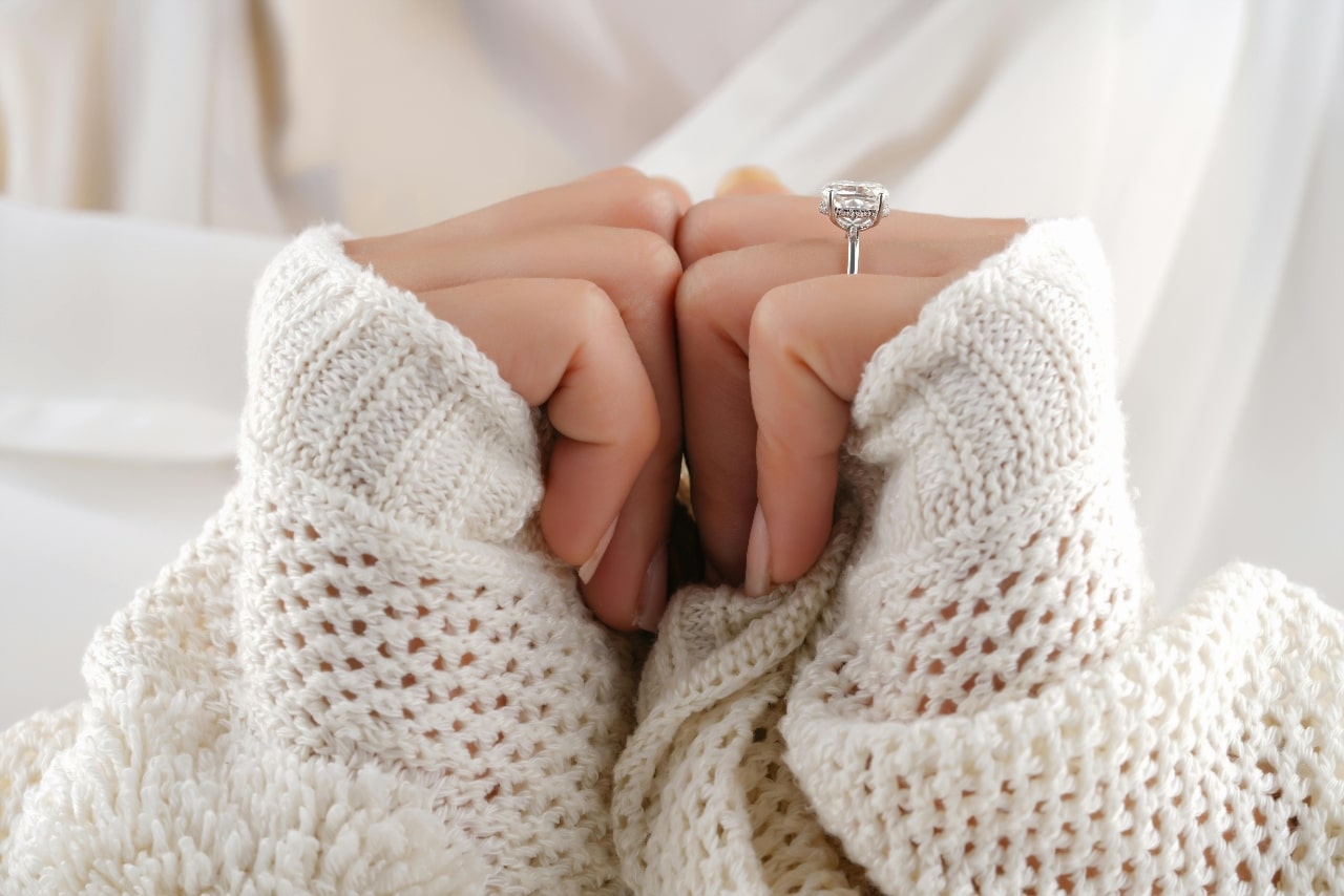 A woman wearing a white sweater and hidden halo engagement ring.