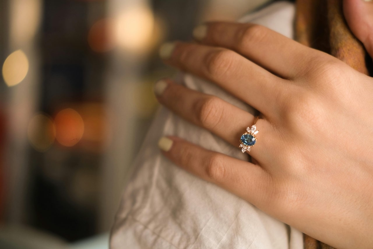 A close up of a woman’s hand adorned with a blue gemstone engagement ring with diamond side stones