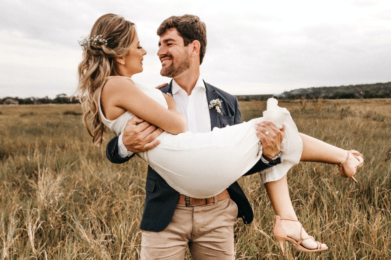 a groom holding his bride standing in a field