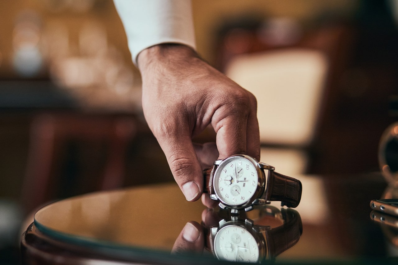 a man’s hand picking up a white and silver watch off of the edge of a round table