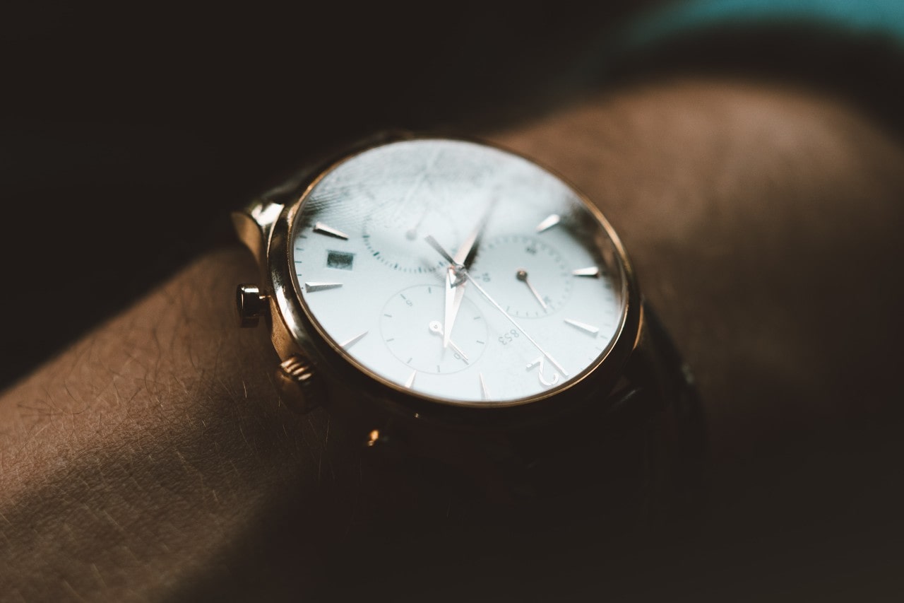 close up image of a gold watch with a white dial, silver hands, and multiple subdials