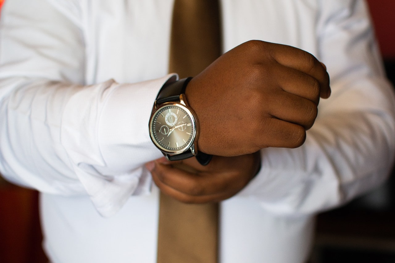 image of a man putting on a gold watch with a metallic bronze dial and black leather strap