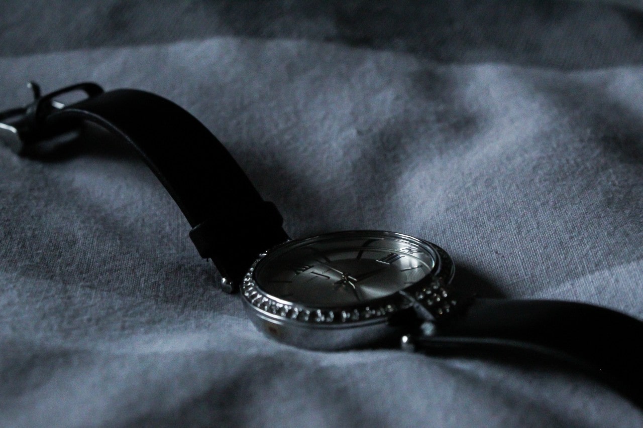 a silver watch with a black leather strap lying on a piece of white linen cloth