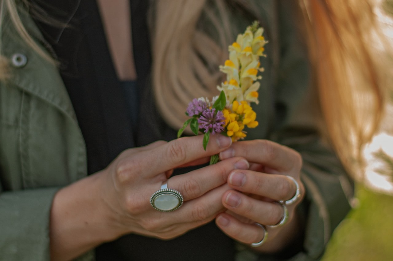 Hands clad in fashion rings holding some wildflowers on a warm spring day.