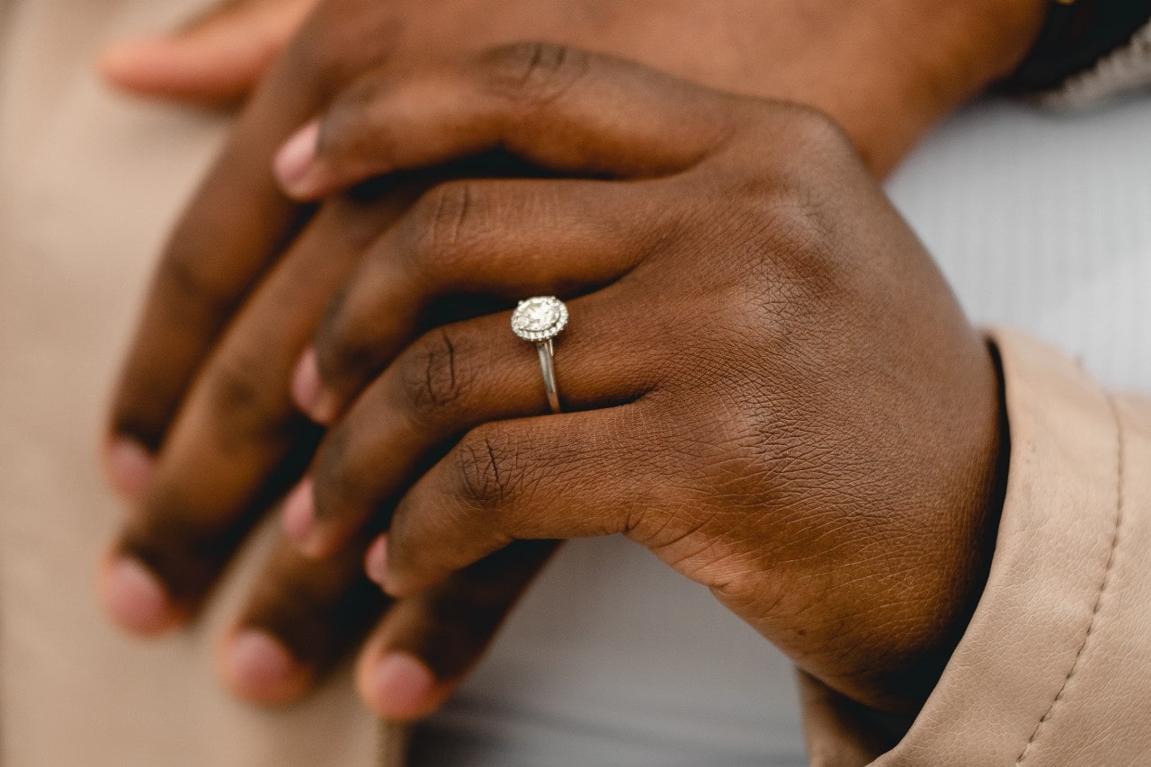 a couple holding hands, the woman wearing an oval cut halo engagement ring