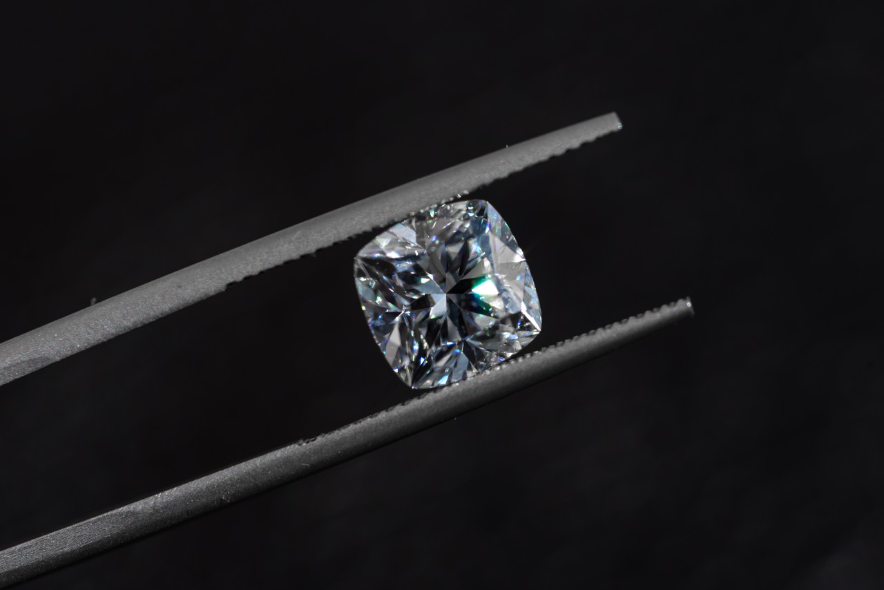 A close-up of a princess cut diamond being held with a pair of pliers.