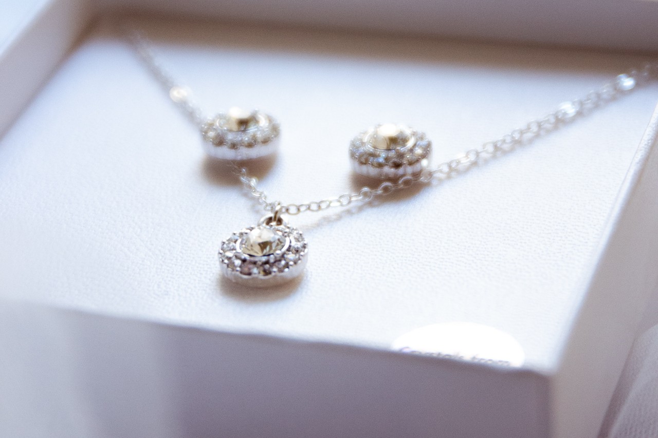A diamond necklace with three separate diamond halo accents, resting on a white surface.