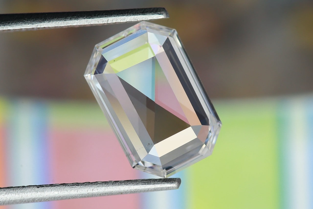 A close-up image of a tweezer holding an emerald cut diamond