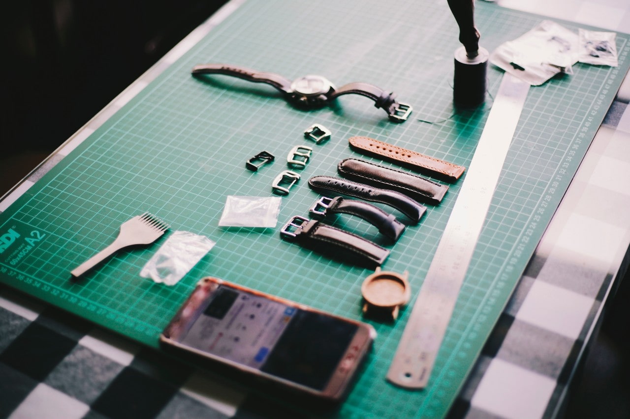 A close up of a working table with several leather straps of the wrist watch, smartphone and ruler.