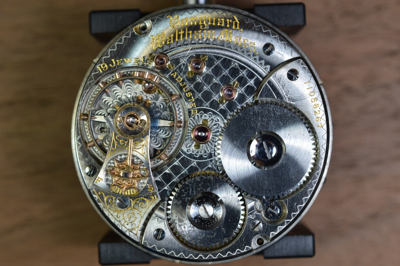 A detailed close-up of a mechanical watch movement shows engraved plates, gears, and ruby jewels.
