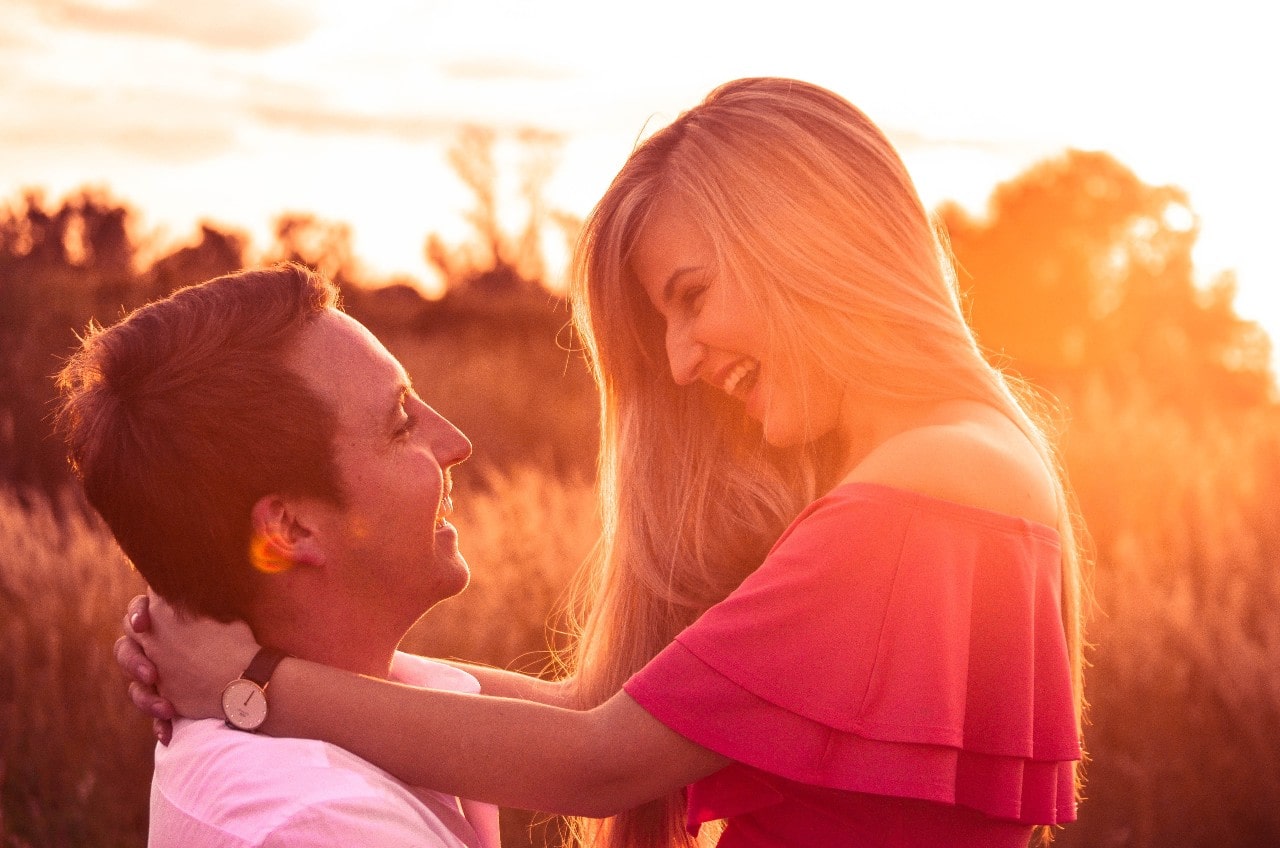 A couple of a date at sunset; the woman has a luxury watch on, the couple smile at each other as they embrace