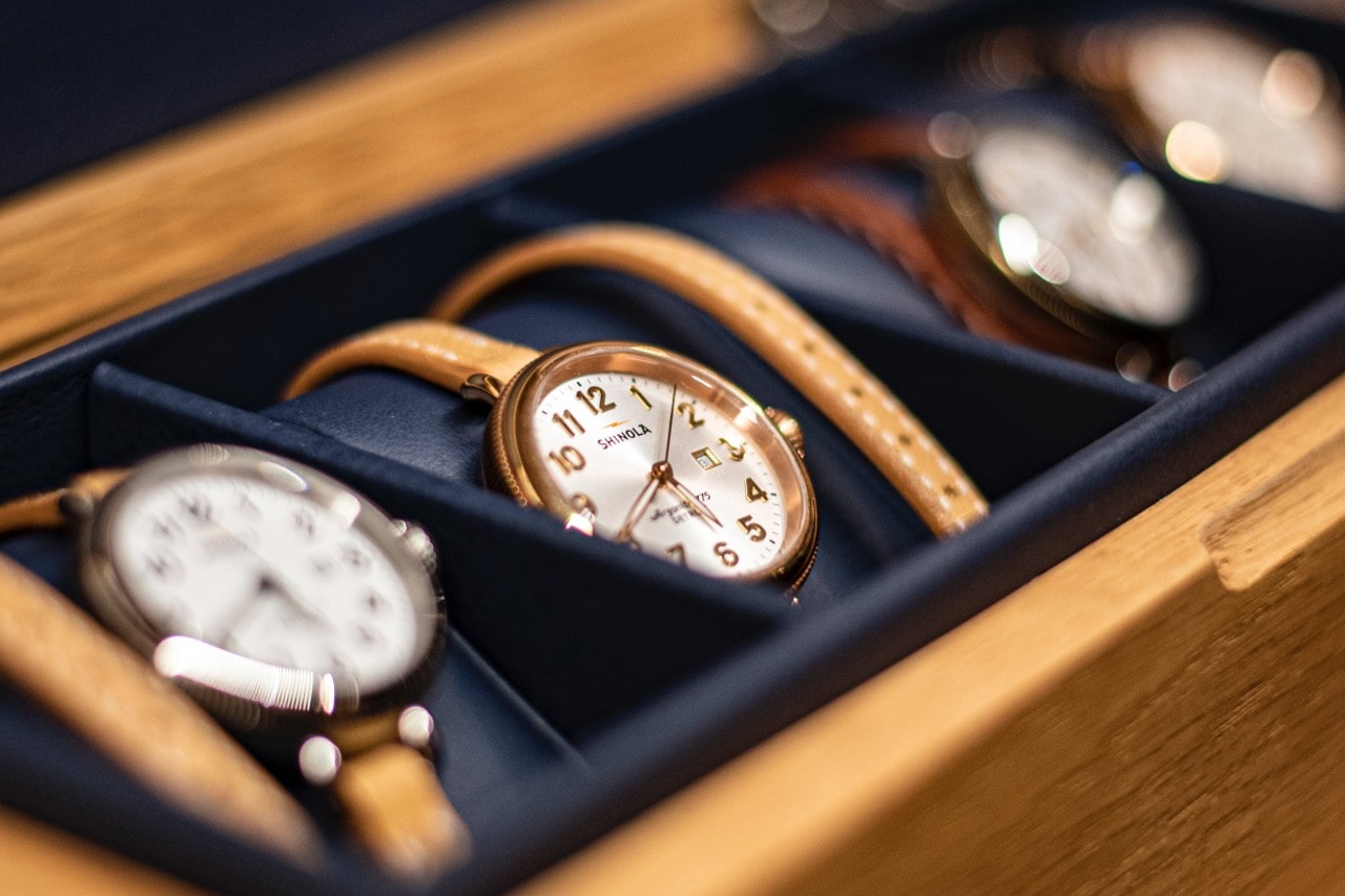 A wooden watch box holds several classic wristwatches with tan leather straps, with a focus on a center timepiece.