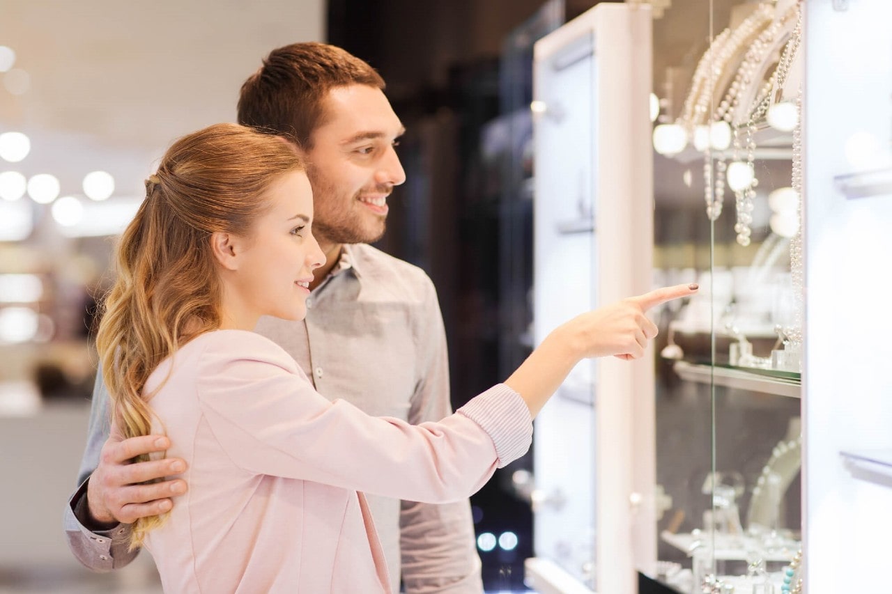 A happy young couple window shopping for jewelry, the woman indicating a piece of jewelry she likes.