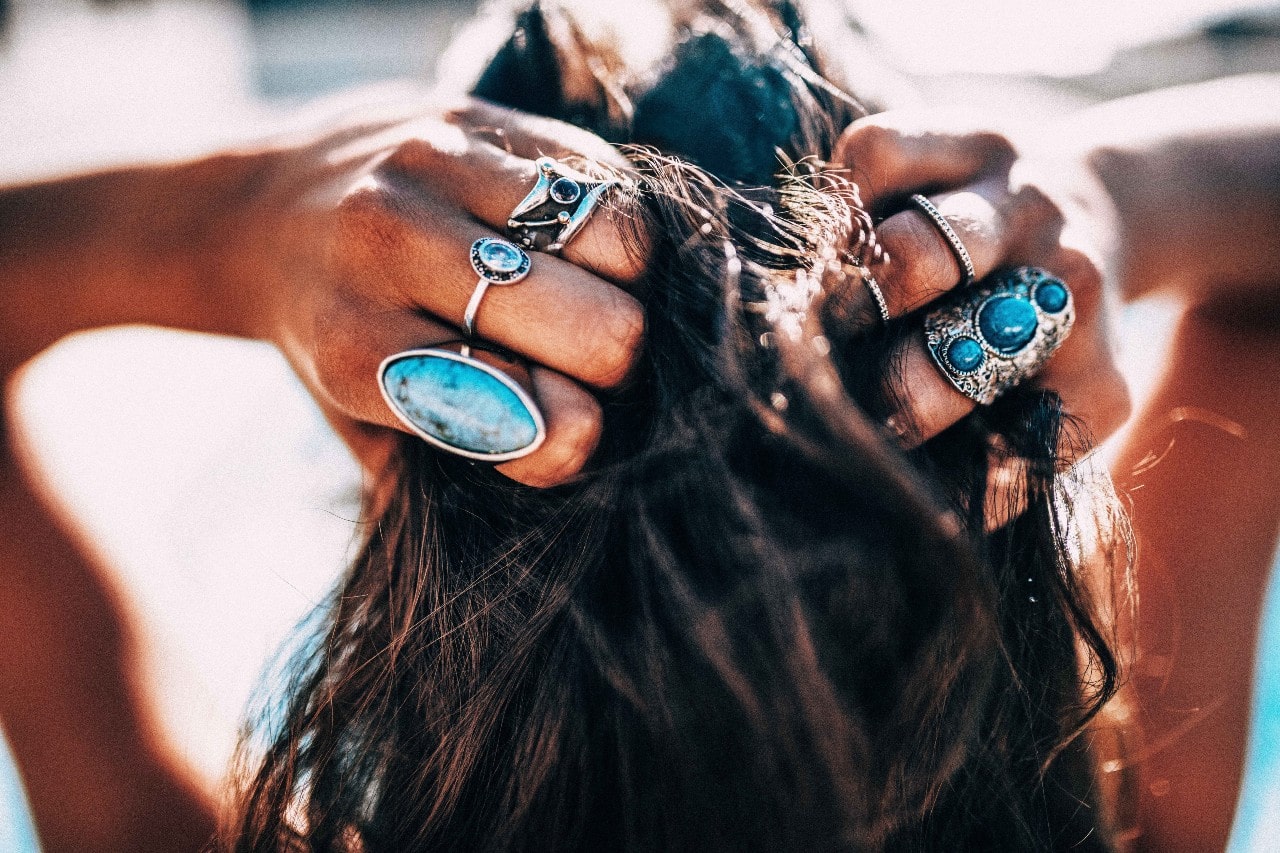 A woman with silver and turquoise rings her fingers through her hair.