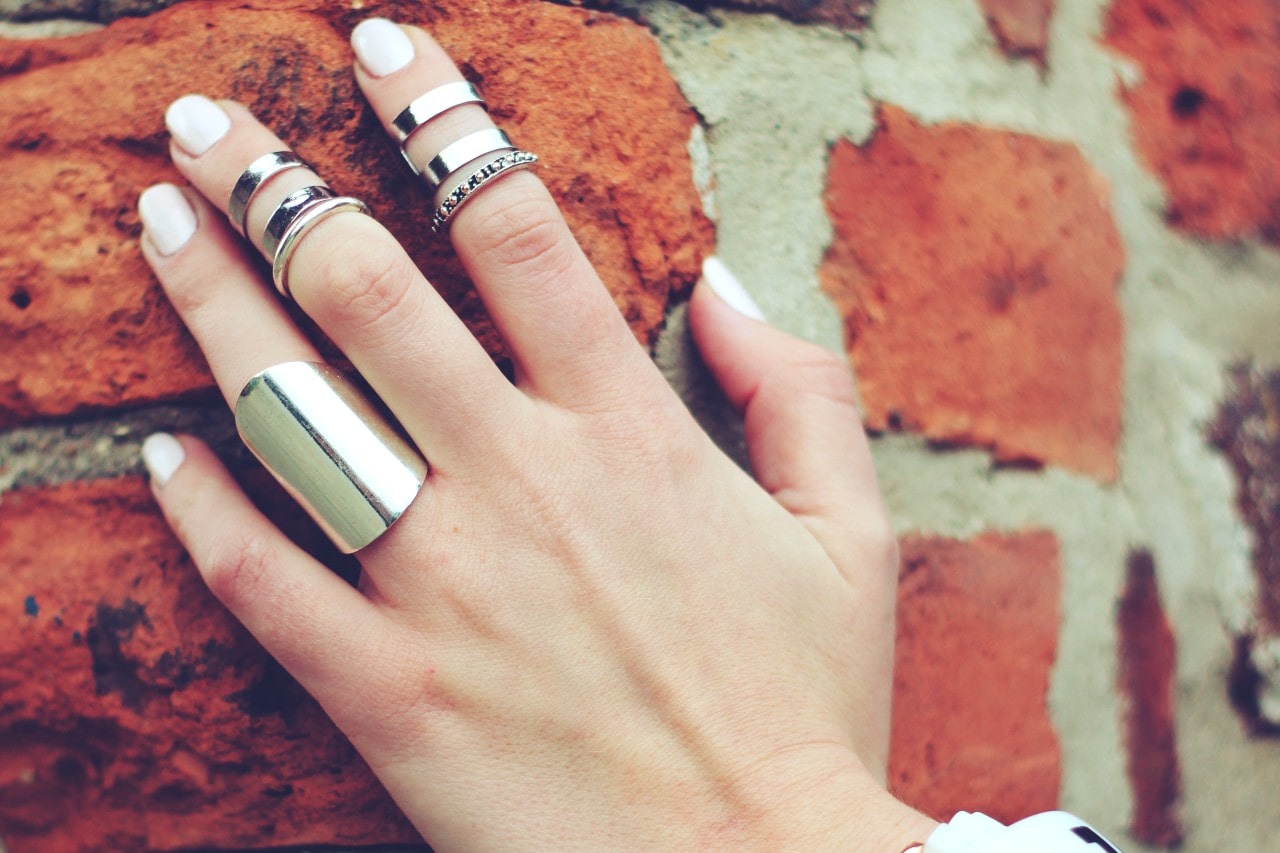A woman rests her hand on a brick wall with an ensemble of silver rings.