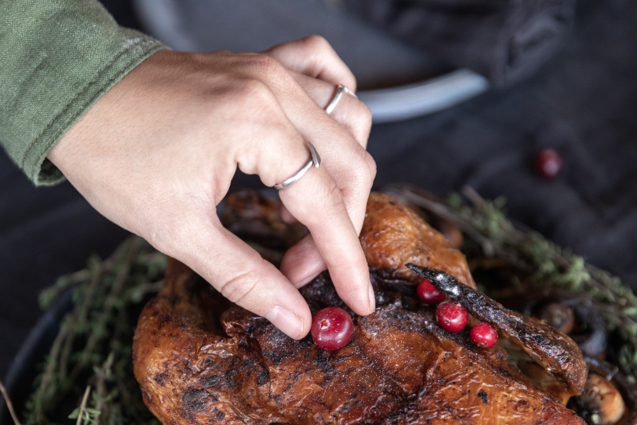 A woman wearing rings places a cranberry on a roasted turkey.