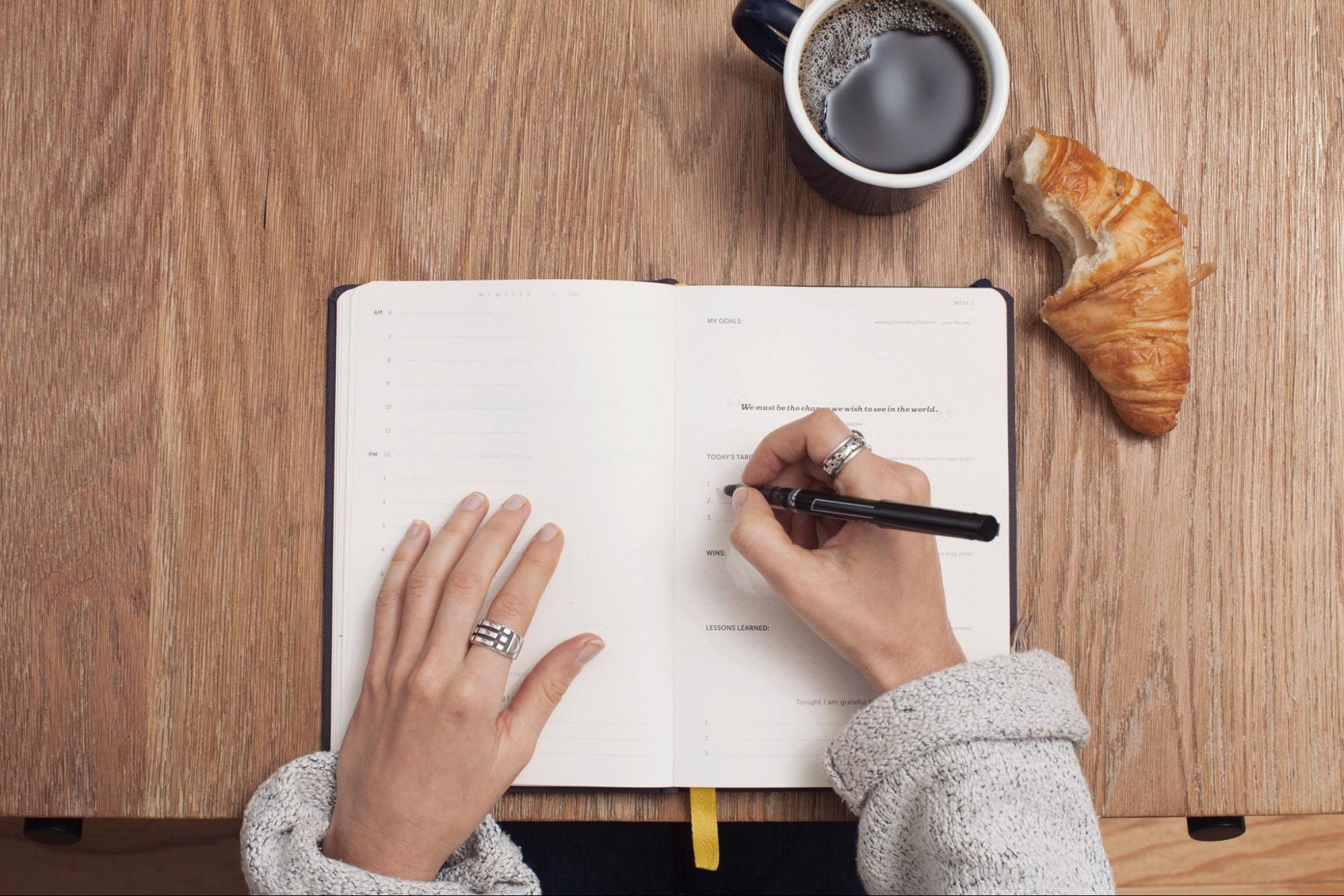 A woman with rings eats breakfast while journaling.