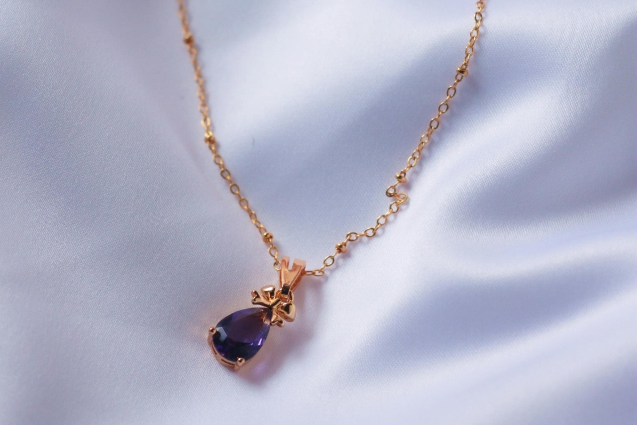 A delicate rose gold necklace with an amethyst pendant, delicately displayed on white satin.