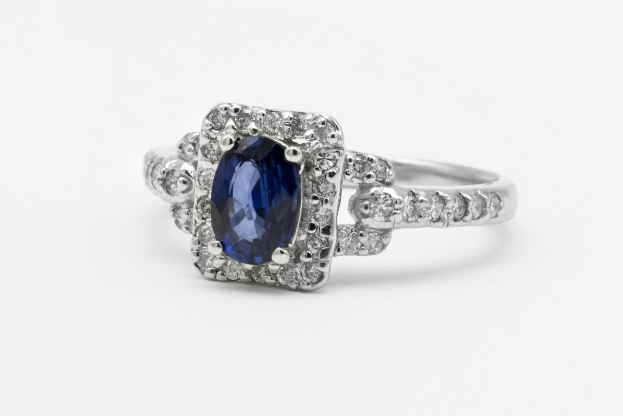 An ornate white gold engagement ring with a square halo and oval cut sapphire center stone.