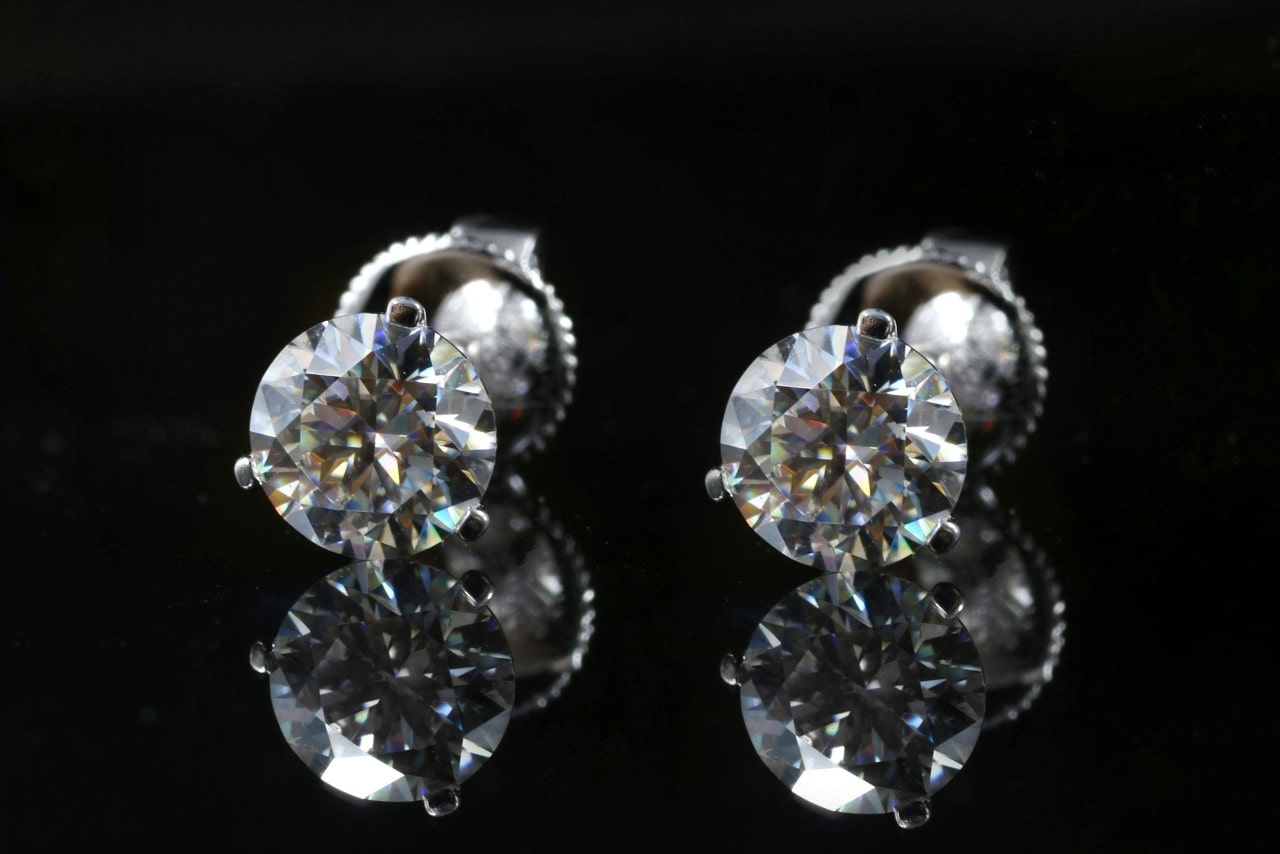 A close-up of a radiant pair of diamond stud earrings on a black backdrop.