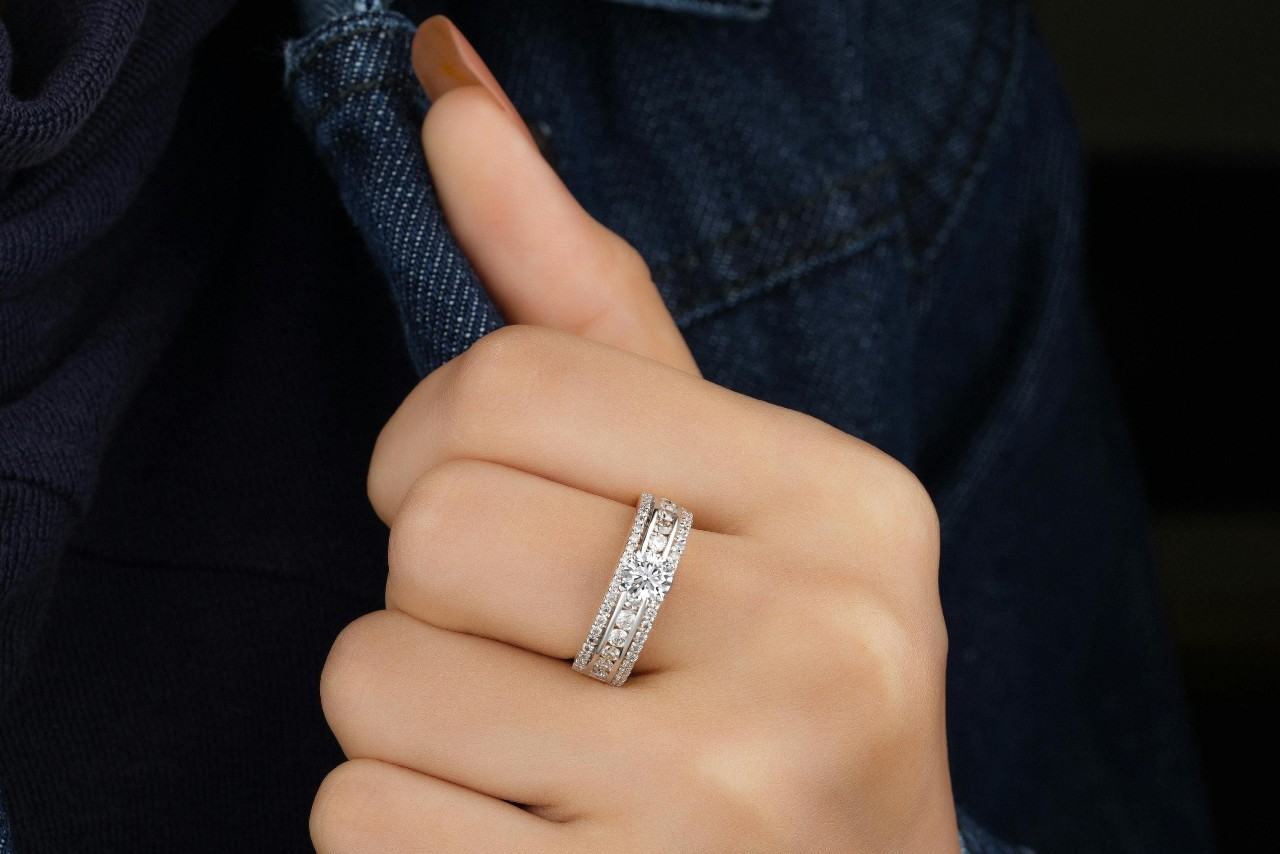 A close-up of a woman’s hand against a dark denim jacket, an elegant and detailed ring on her finger.