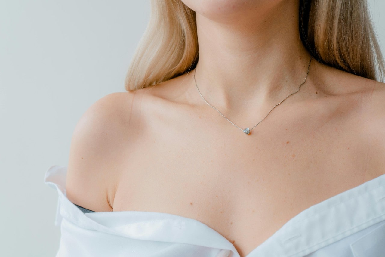 A close-up of a young woman wearing an off the shoulder blouse, a delicate diamond pendant adorning her decolletage.