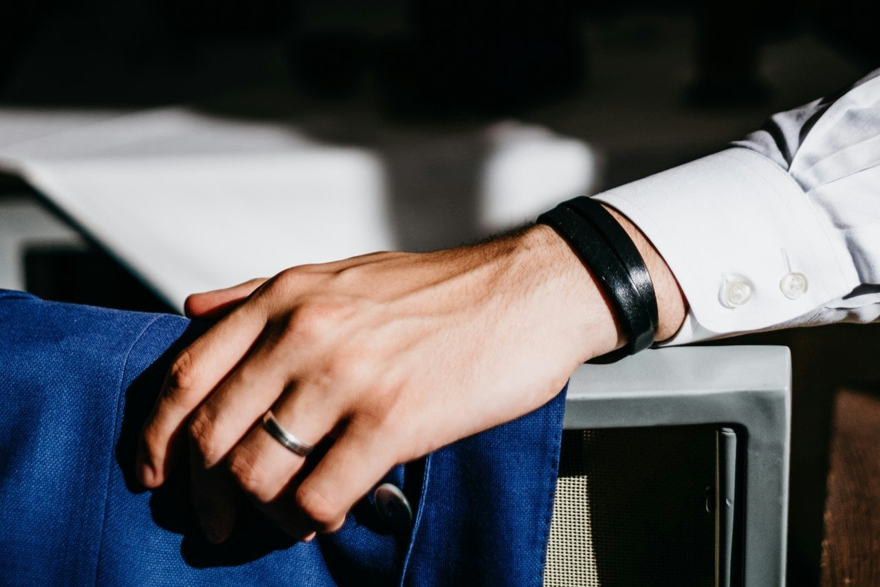 Close-up of a groom's hand wearing a wedding band and a black leather bracelet.