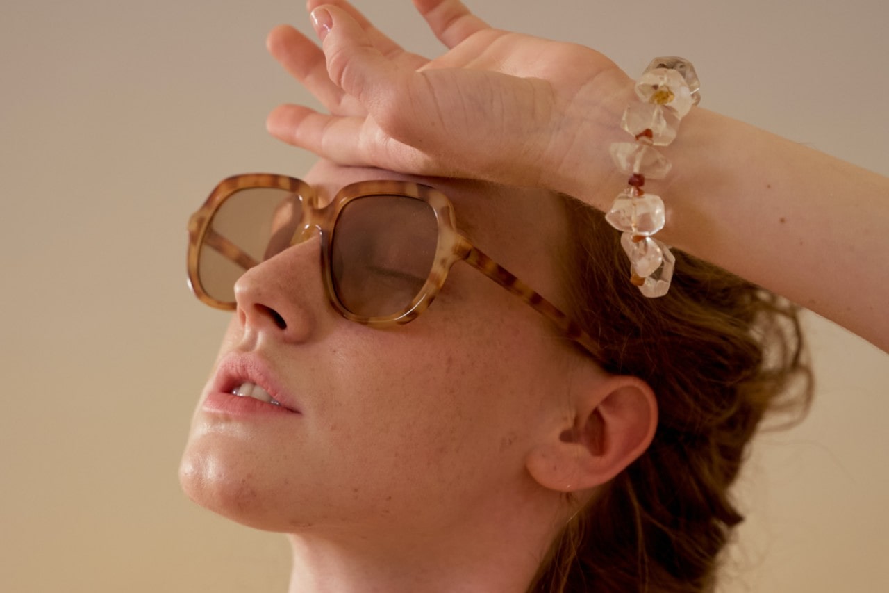 A woman lounging wears sunglasses and a seashell-beaded bracelet.