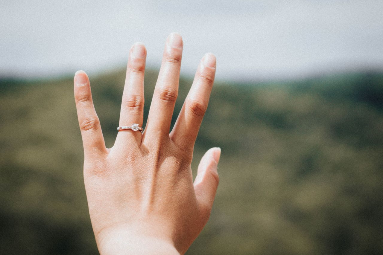 an image of a woman holding out her hand and wearing an engagement ring with blurred foliage in the background