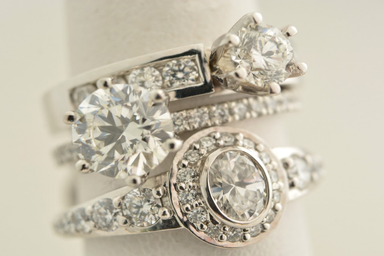 three silver and diamond engagement rings stacked on each other with a white background