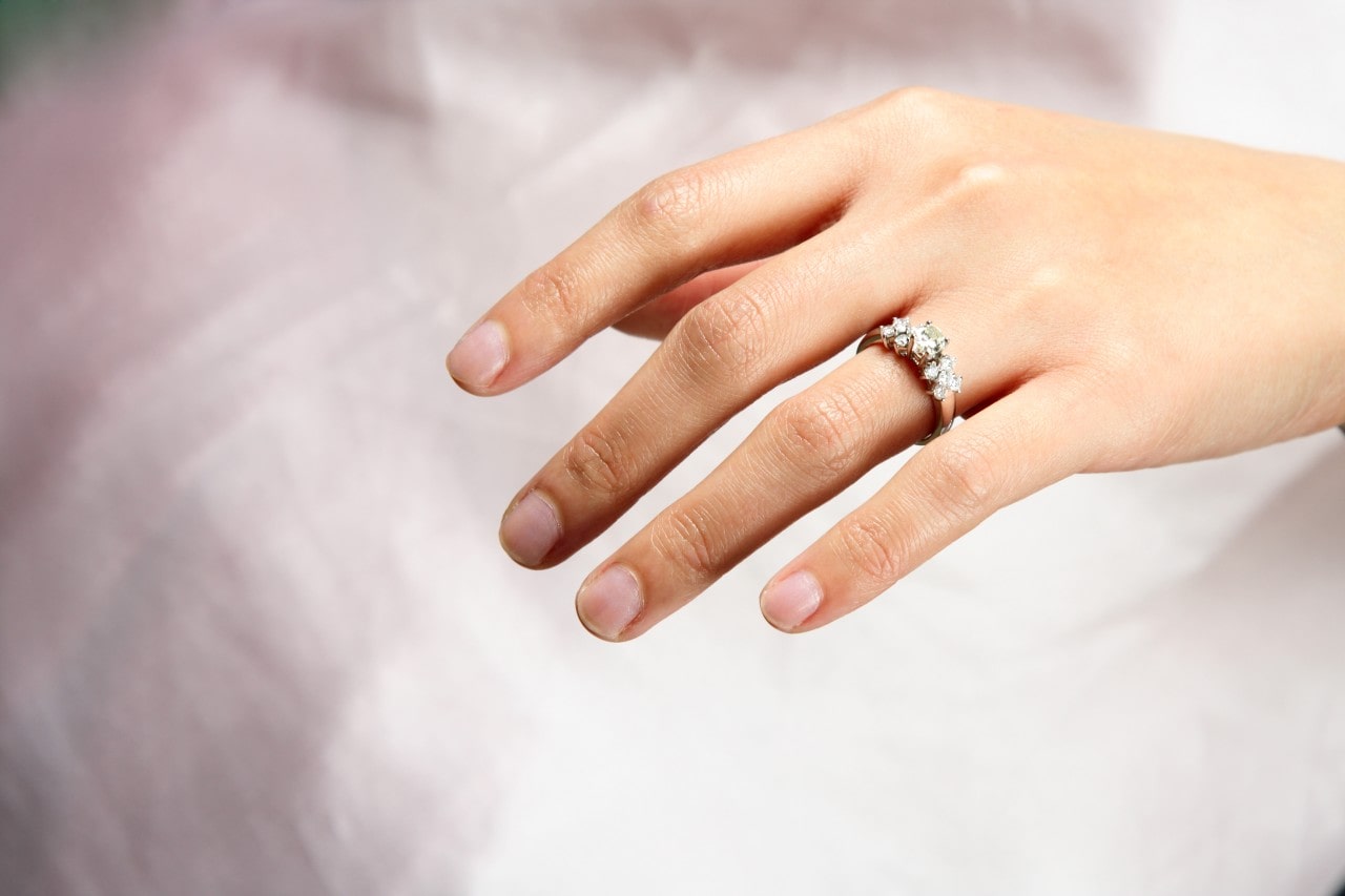 an extended hand wearing an engagement ring with a white background