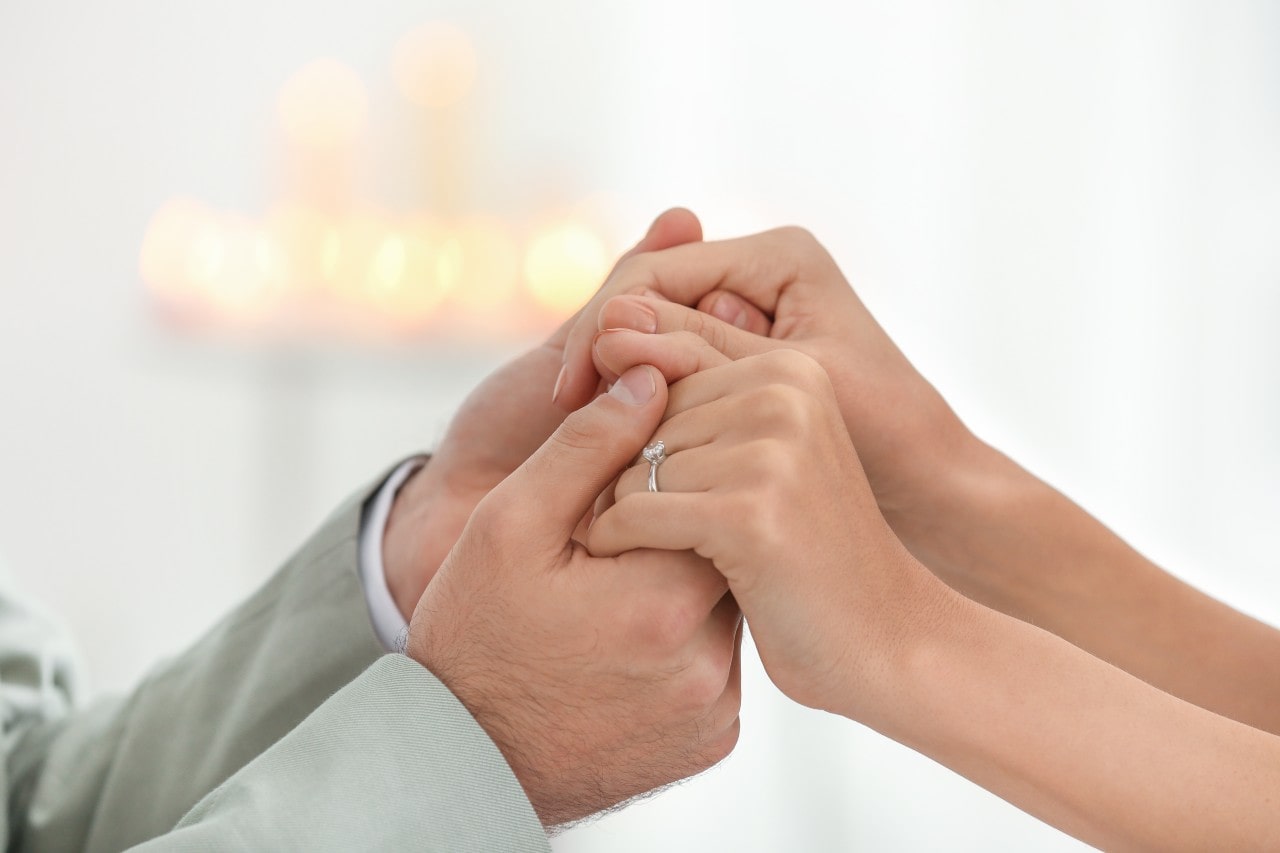 close up of a couple holding hands, the woman wearing a diamond engagement ring