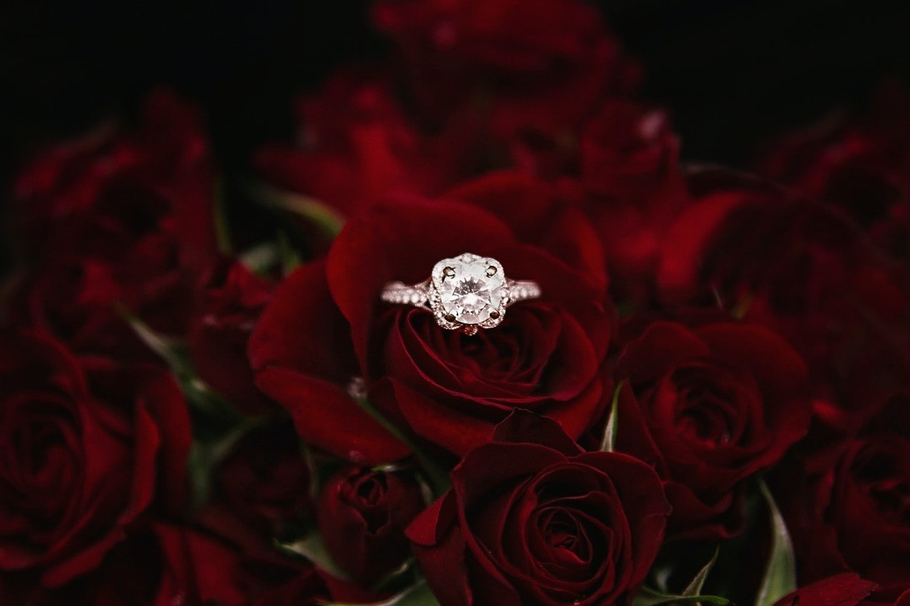 a round cut engagement ring with accent stones on a bouquet of roses